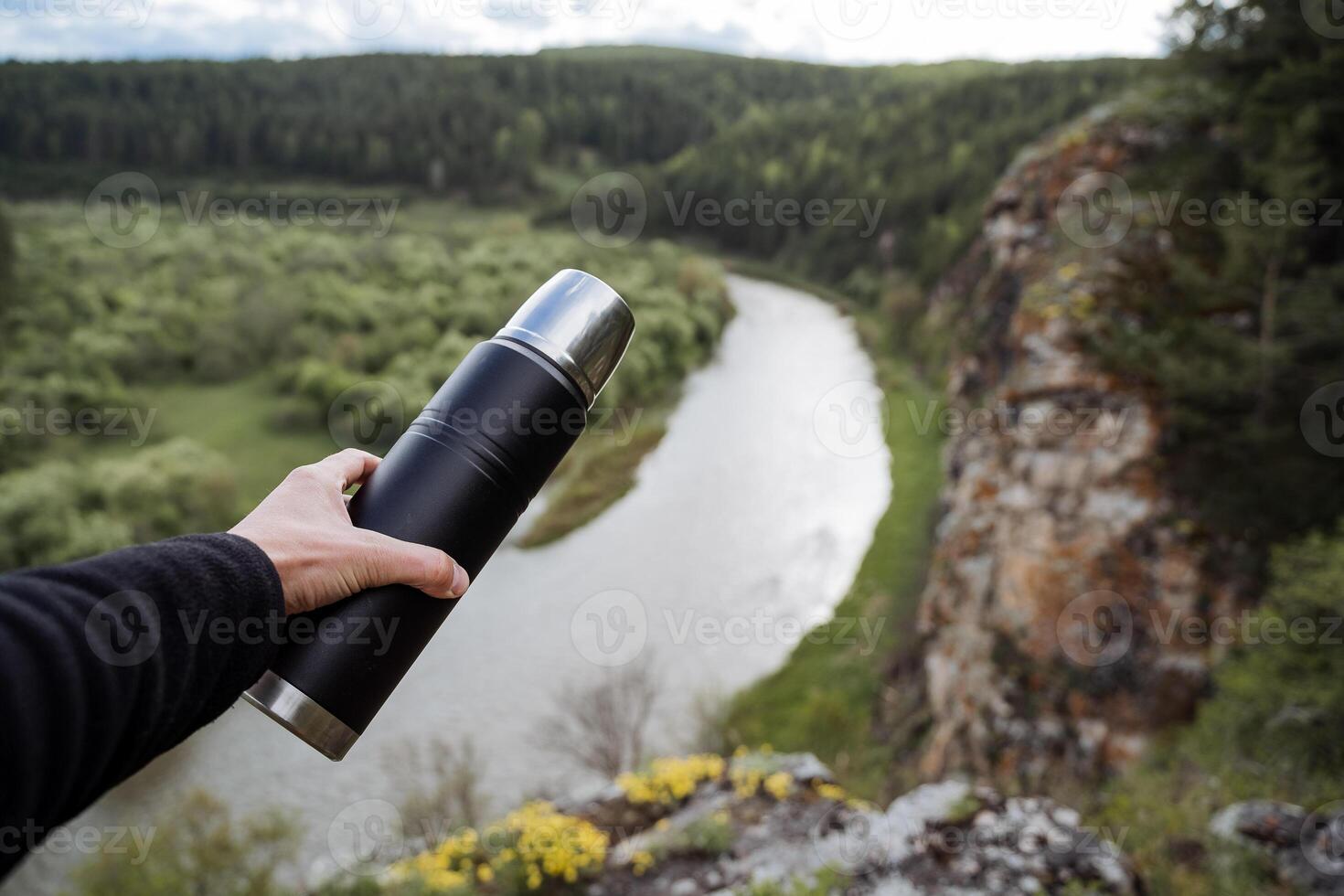 une thermos dans le main de une la personne contre le Contexte de une rivière, randonnée dans le montagnes, une paysage de montagneux terrain dans Russie, le du sud Oural, le tour de le rivière plier. photo