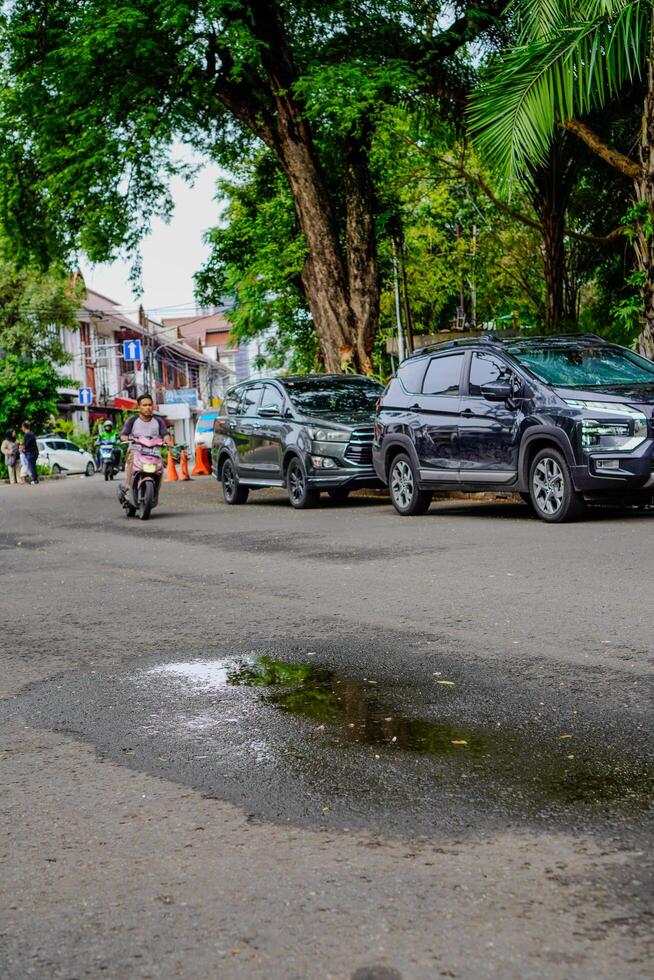 central Djakarta, janvier 30, 2024 - flaques d'eau de l'eau dans le milieu de le Autoroute, avec voitures garé sur le côté de le route. photo
