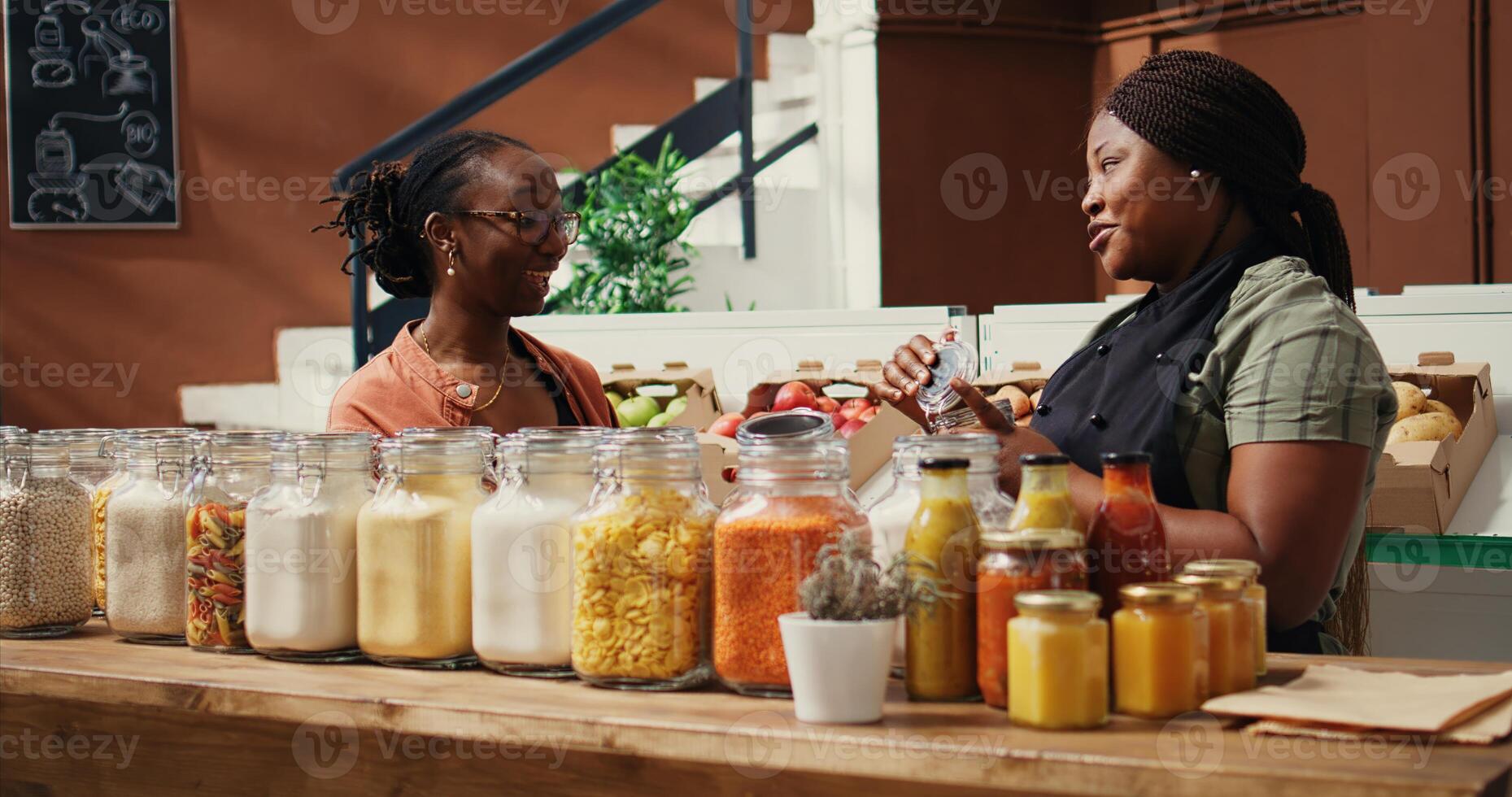 africain américain vendeur donnant nourriture échantillon à client, en présentant Nouveau fait maison collations avec Naturel ingrédients. végétalien femme en essayant en dehors marché des produits avant achat. ordinateur de poche tir. photo