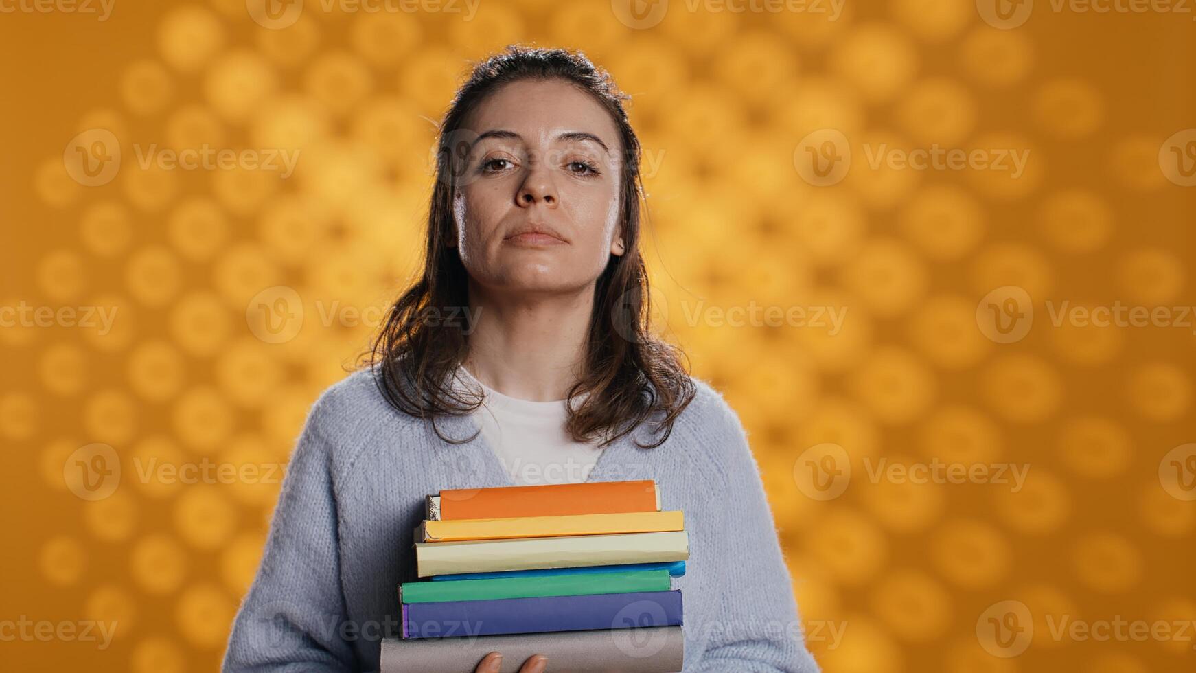 portrait de optimiste femme en portant pile de livres, profiter en train de lire loisir pour divertissement fins. radiant rat de bibliothèque avec empiler de des romans dans bras profiter loisir temps, studio arrière-plan, caméra b photo