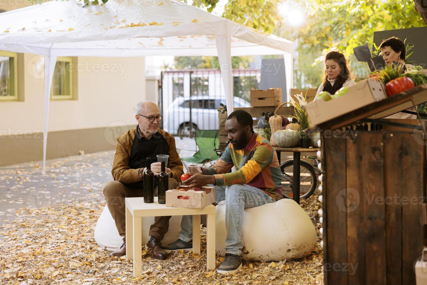 africain américain client séance à une Les agriculteurs marché table avec une local fournisseur, ayant fait maison du vin. noir Masculin client visite un biologique l'automne Festival et profiter du vin et nourriture dégustation. photo