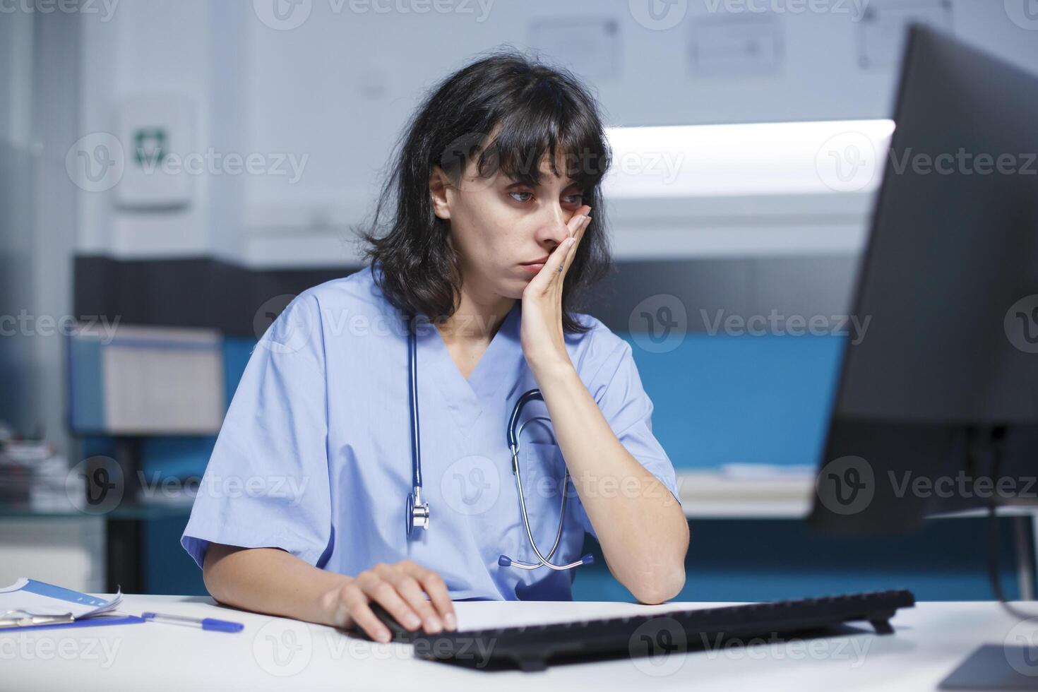 dans bureau, médical assistant les usages une ordinateur et Souris pour le soins de santé système. tandis que travail en retard à nuit, le infirmière est jetant un coup d'œil à le moniteur écran pour soutien et assistance. photo