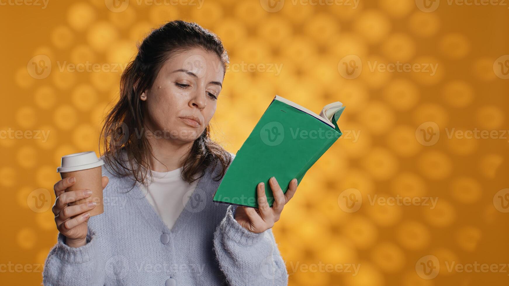 fatigué femme en train de lire livre, en portant tasse de café, isolé plus de studio Contexte. épuisé rat de bibliothèque profiter roman et caféine boisson, manquant énergie, en difficulté à rester éveillé, caméra b photo