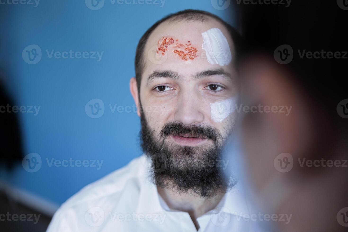 acteur attendre dans maquillage département à recevoir faux du sang blessures, en train de préparer pour film scène. homme avoir costumé comme zombi monstre par maquillage artiste appliquant sang produits de beauté photo