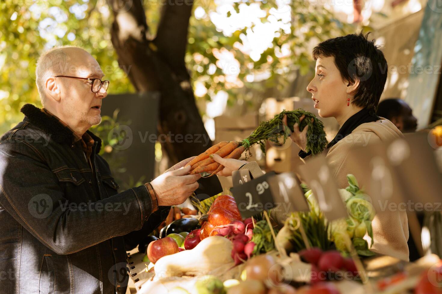 Jeune vendeur donnant fraîchement récolté biologique carottes à Les agriculteurs marché stalle stand. personnes âgées client achat localement grandi des légumes de femelle marchande à marché vert rester. photo