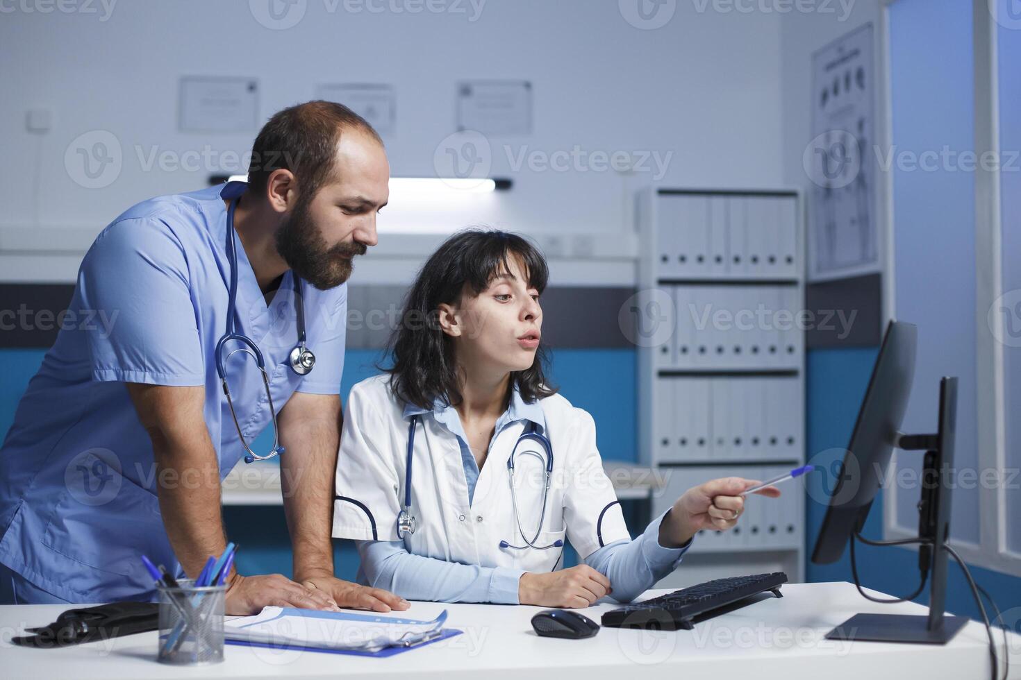 caucasien médical Personnel dans bleu gommages et laboratoire manteau collaborer numériquement dans une clinique bureau. elles ou ils utilisation une ordinateur pour conférence, montrant information et faire des gestes tandis que La technologie domine chambre. photo