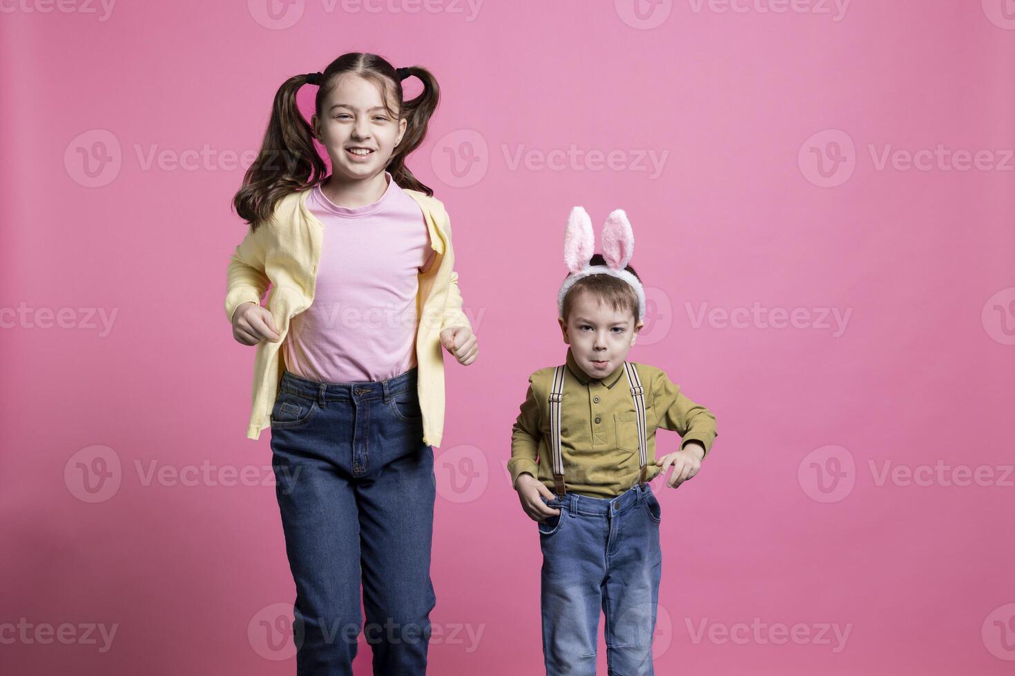 frère avec lapin oreilles et sœur sauter autour dans le studio, peu les enfants étant content à propos Pâques temps fête. adorable Fratrie rebondir comme lapins contre rose Contexte. photo