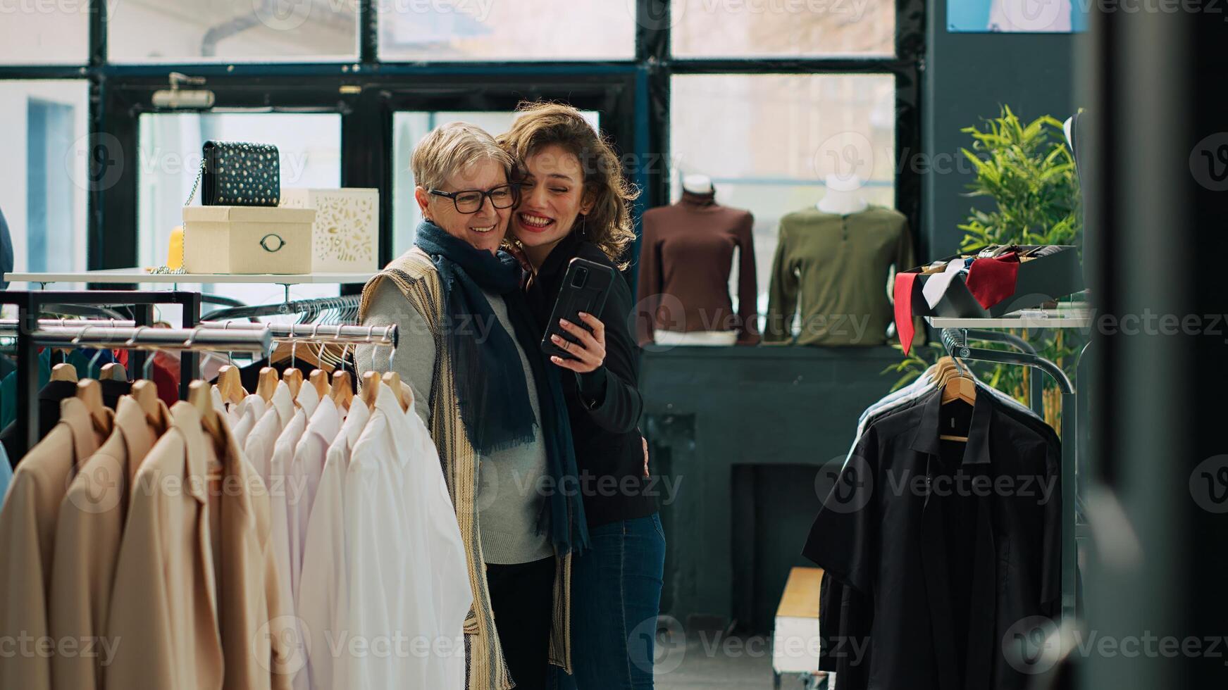 Sénior femme et sa fille prendre Photos dans département magasin, profiter journée de achats pour vêtements. souriant les clients avoir amusement avec selfies dans une mode salle d'exposition, commercial activité. caméra un.