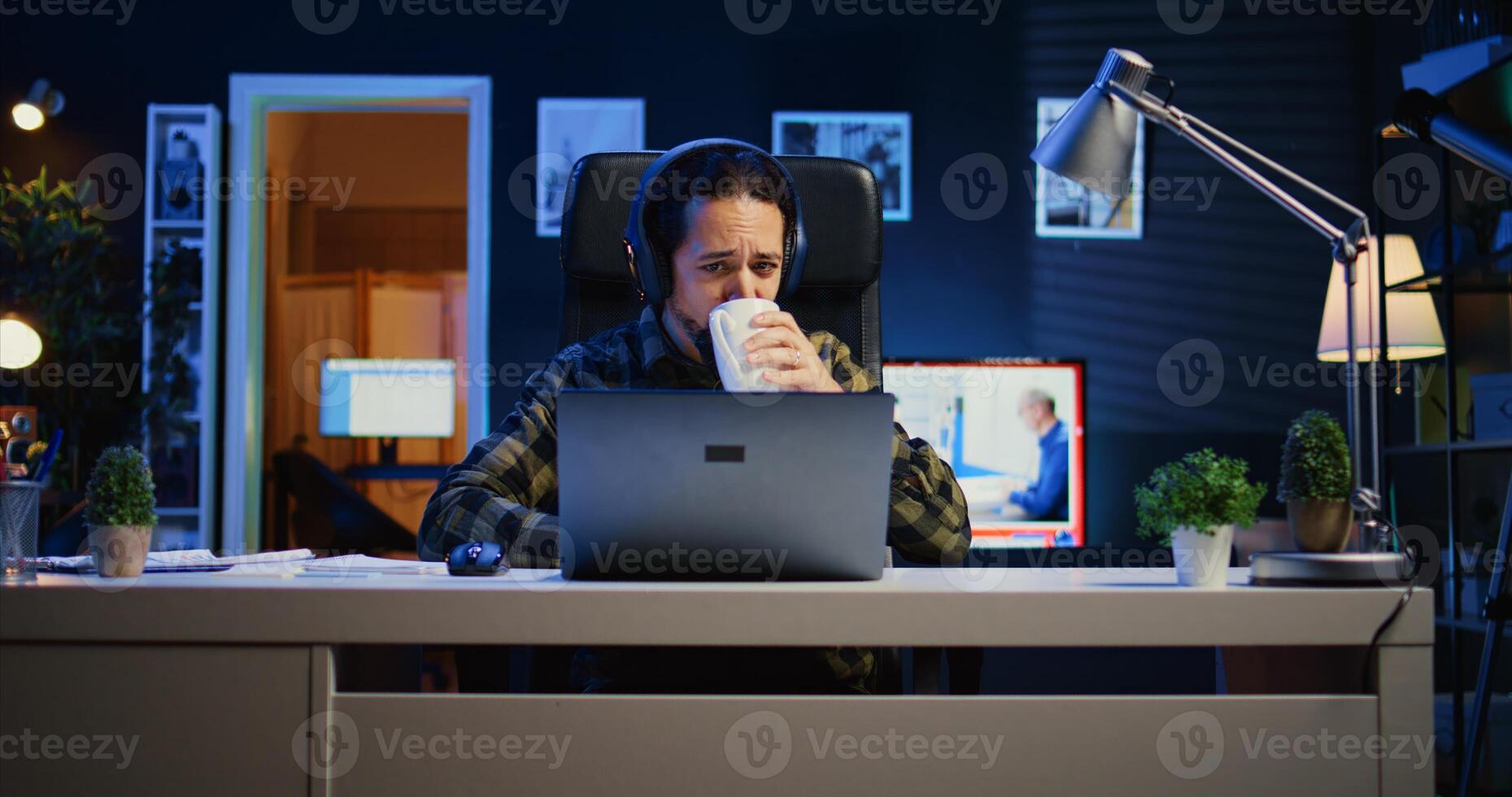 caucasien homme séance sur chaise à Accueil Bureau bureau dans néon illuminé appartement, travail et écoute musique. télétravailleur portant écouteurs dans rgb allumé vivant chambre, Faire le sien emploi à distance photo