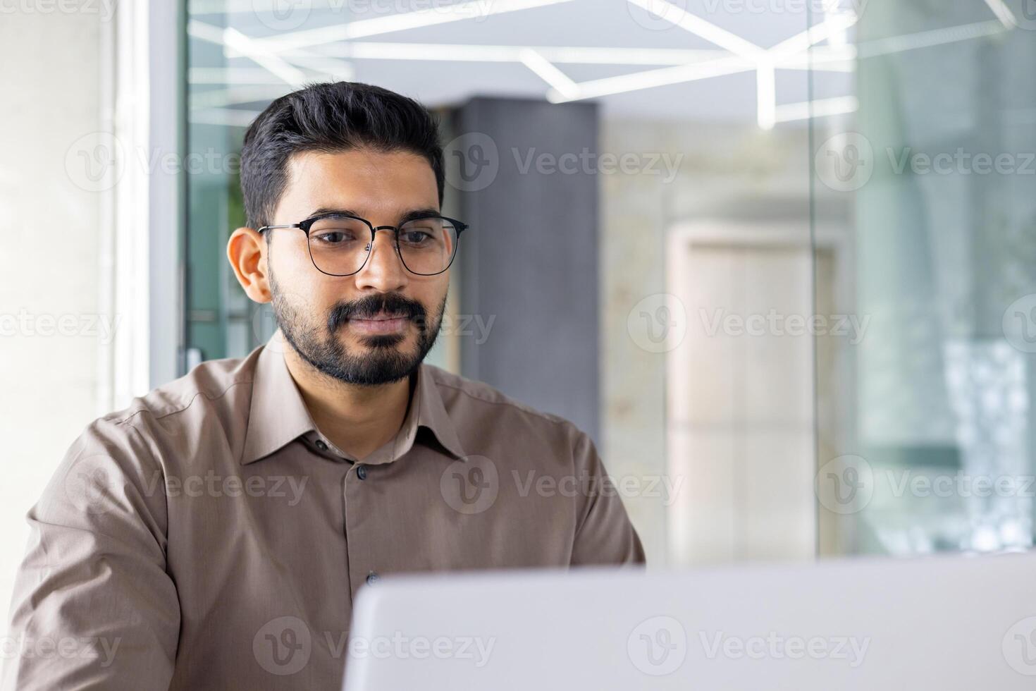 concentré Indien homme d'affaire en utilisant une portable à le sien Bureau espace de travail, incorporant professionnalisme et dévouement. photo