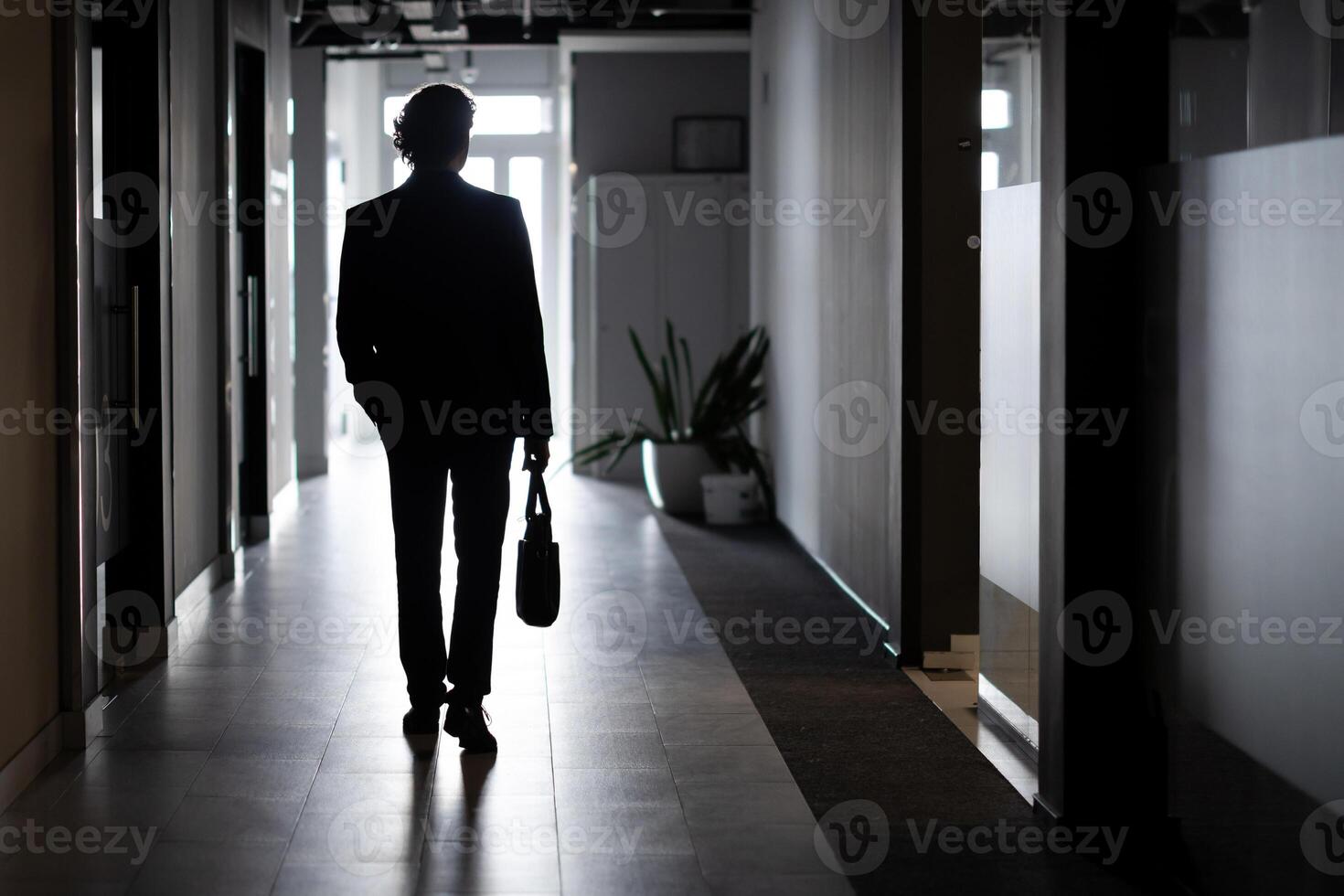 silhouette de une homme d'affaire dans plein hauteur, une homme à l'intérieur le Bureau des promenades le long de le couloir, entreprises, un employé dans une affaires costume. photo