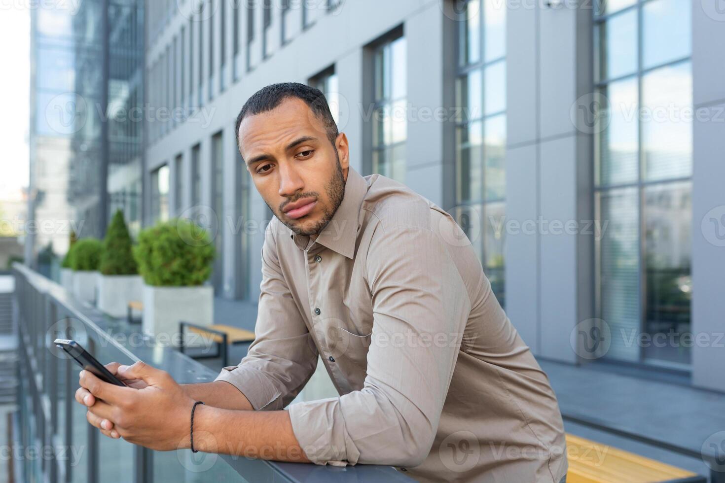sérieux en pensant homme d'affaire à l'extérieur Bureau bâtiment méditer décision, africain américain ouvrier triste en portant téléphone dans main photo