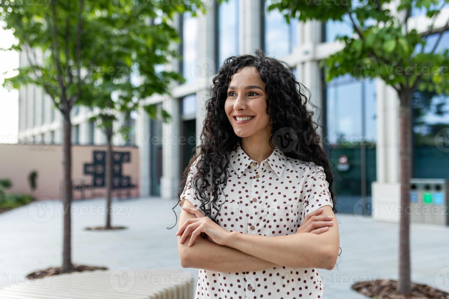 Jeune content hispanique femelle étudiant avec bras franchi à l'extérieur Université Campus souriant avec contentement et à la recherche loin. photo