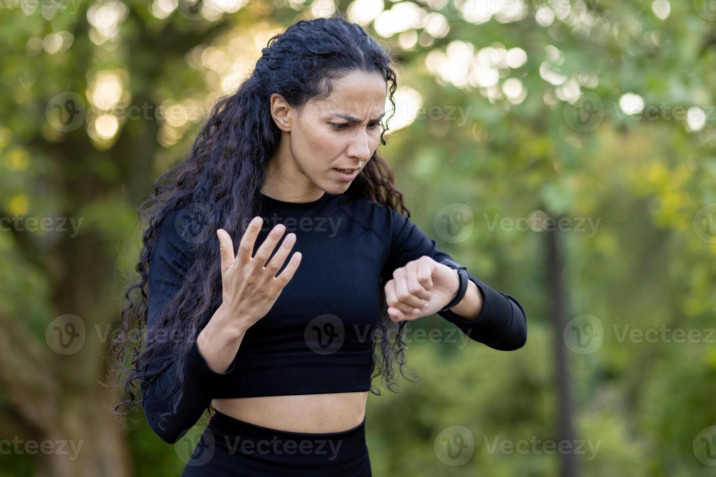 une confus hispanique femme dans faire des exercices tenue chèques sa regarder pendant un exercice session dans une parc, exprimer incertitude et léger frustration. photo