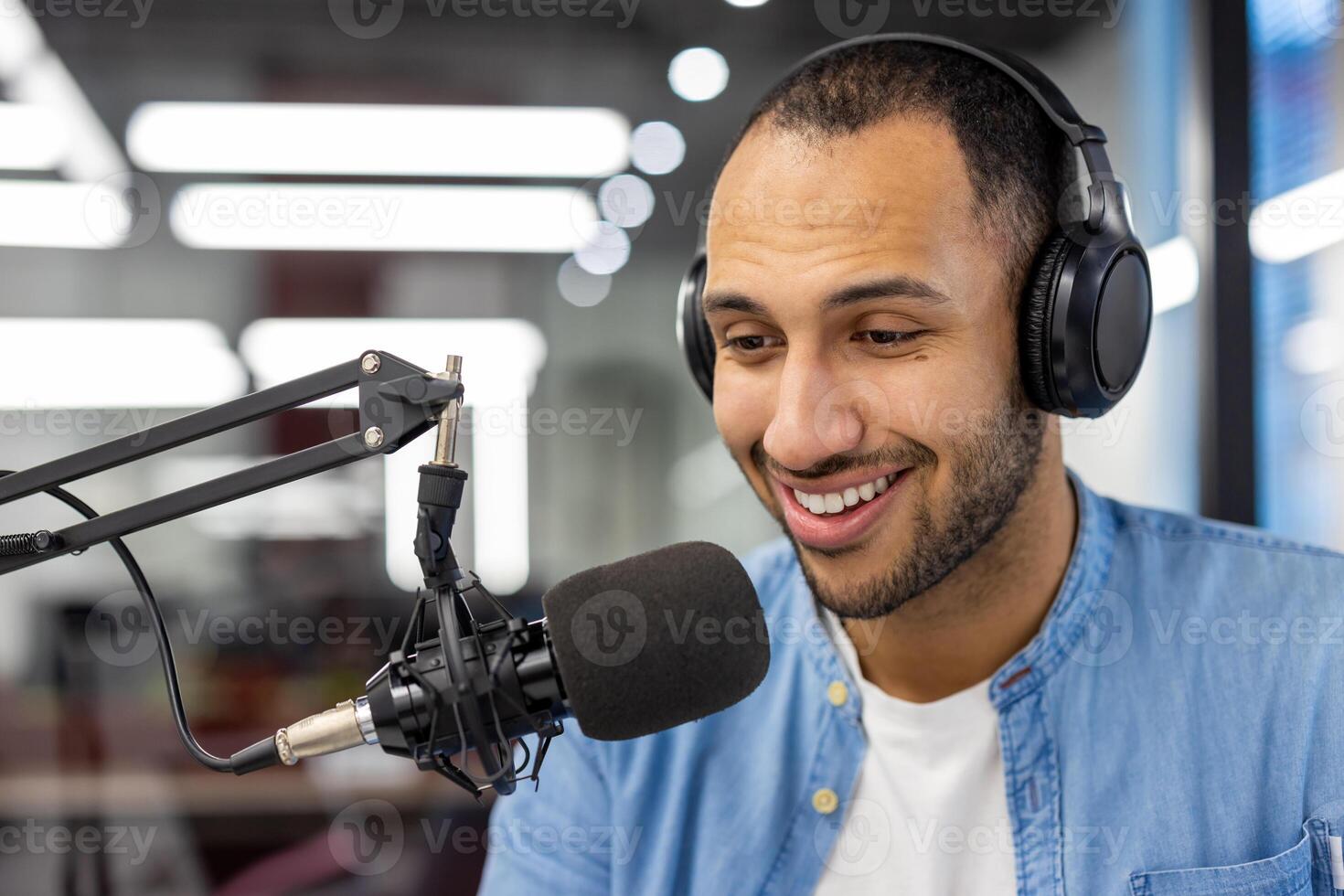 fermer photo de une Jeune souriant hispanique homme dans écouteurs séance dans de face de une bureau avec une microphone dans le Bureau ,et parlant en ligne.