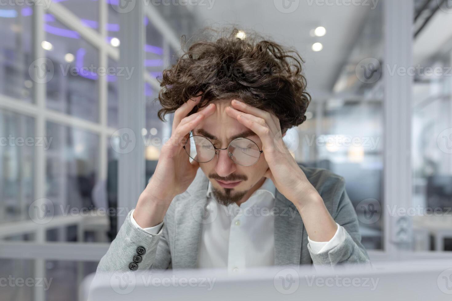 Jeune adulte Masculin Bureau ouvrier montrant panneaux de stress et fatigue, en portant tête dans mains à le sien bureau. professionnel Burnout concept. photo
