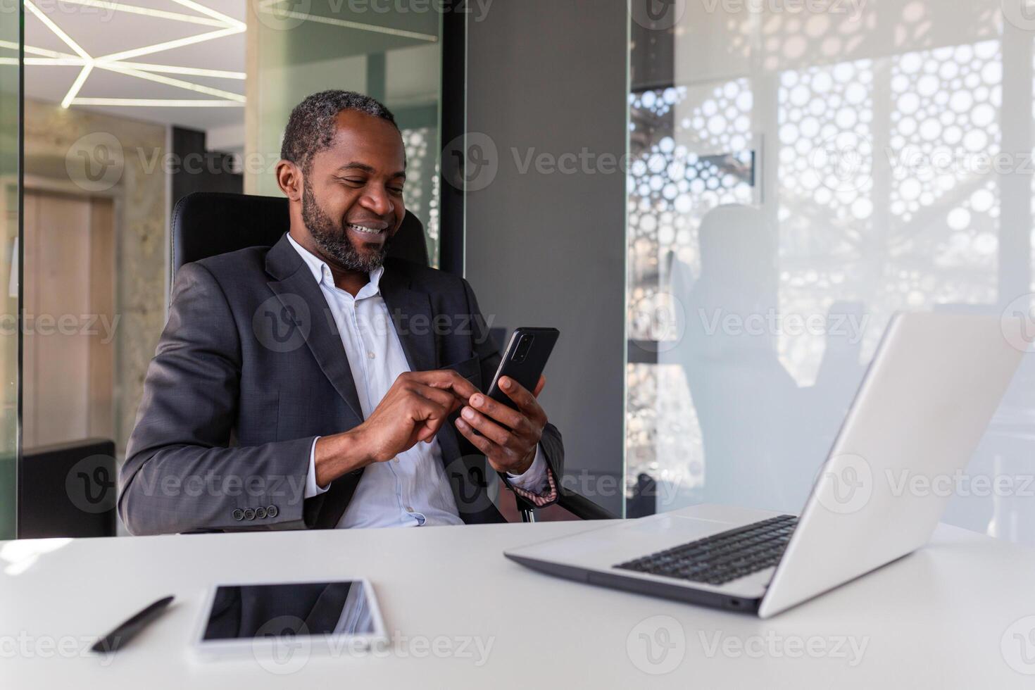 mature expérimenté et réussi africain américain patron à lieu de travail à l'intérieur bureau, Sénior satisfait avec résultats homme d'affaire en utilisant téléphone, en train de lire nouvelles de en ligne app sur téléphone intelligent. photo