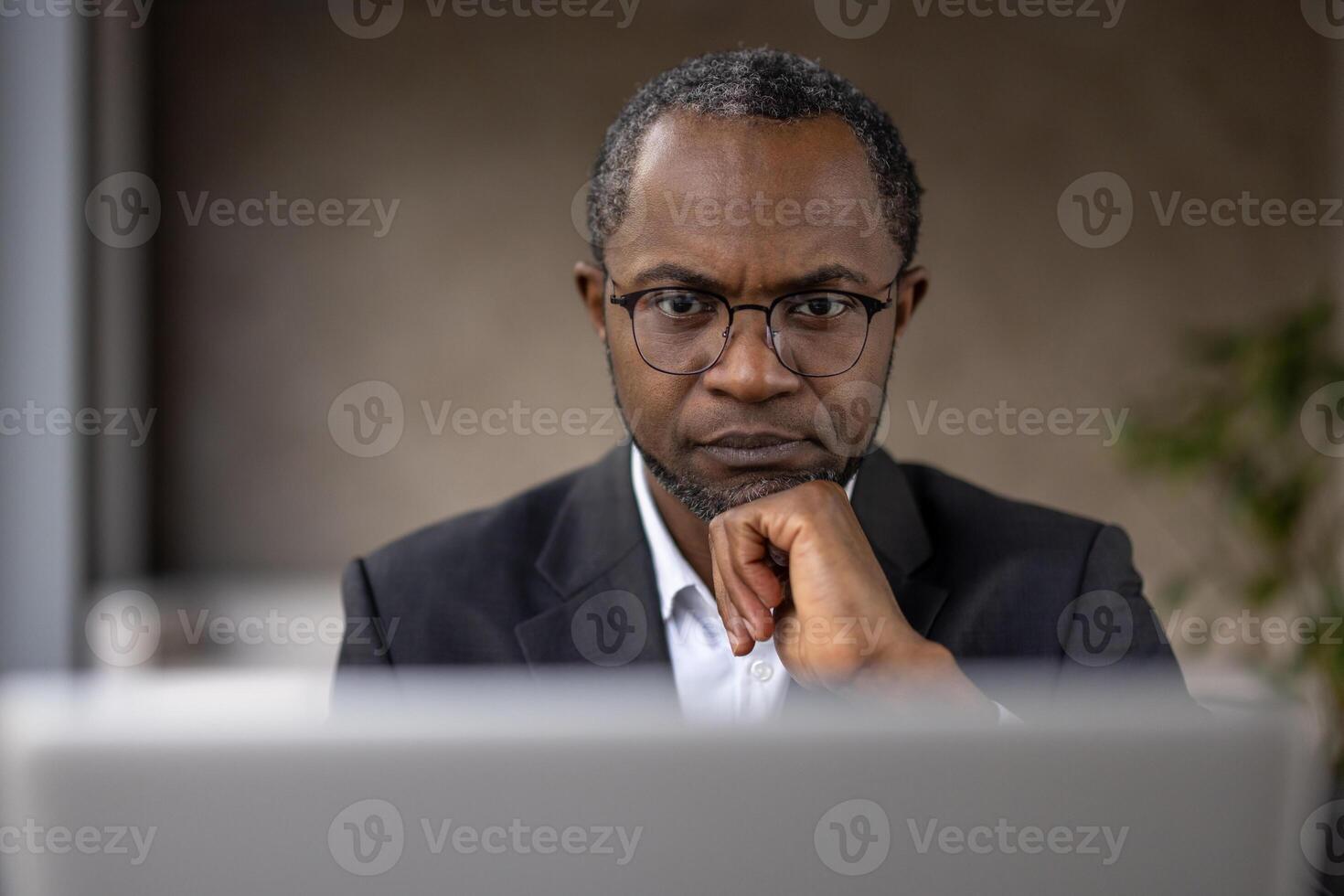 une concentré Afro-américain homme d'affaire dans Bureau tenue travail intensément sur le sien ordinateur portable, affichage professionnalisme et dévouement. photo