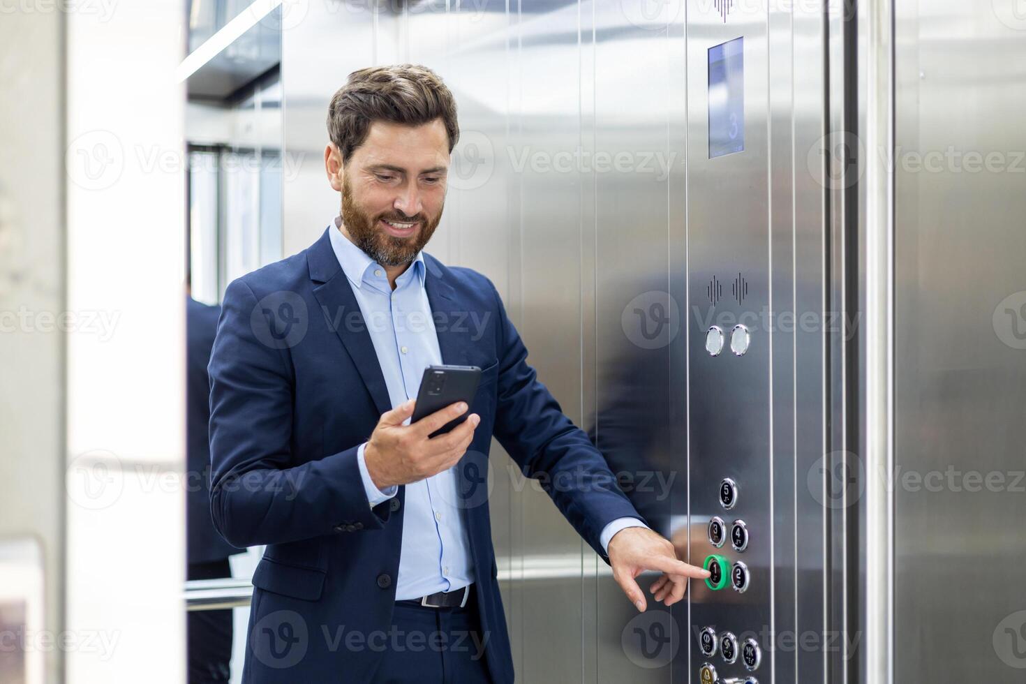 une Jeune souriant homme d'affaire et avocat est permanent dans le ascenseur de un Bureau bâtiment et pressage le faux bouton tandis que en utilisant une mobile téléphone. photo