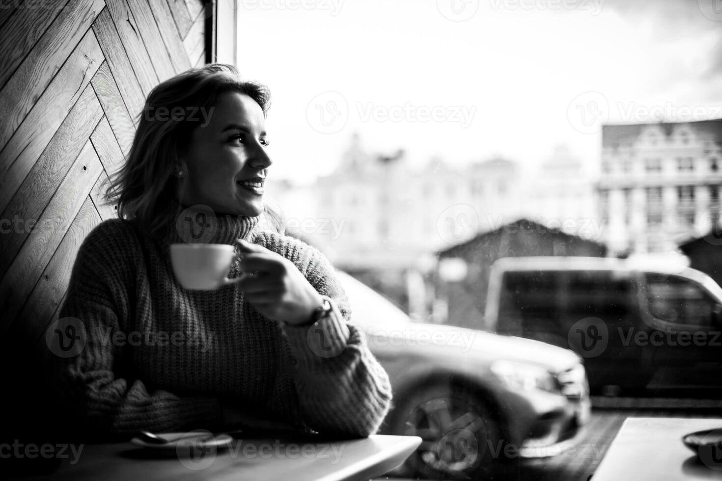 femme profiter café par fenêtre dans ville café. une contenu femme est assis à une café tableau, souriant et regarder en dehors le fenêtre avec une tasse de café dans main. le Urbain scène à l'extérieur Caractéristiques une garé auto. photo