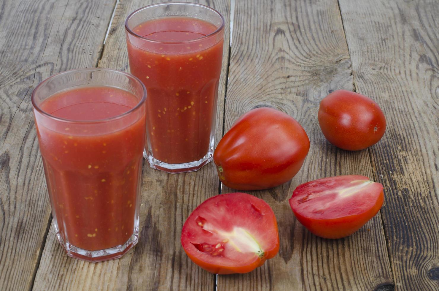 verres avec du jus de tomates rouges mûres sur table en bois photo