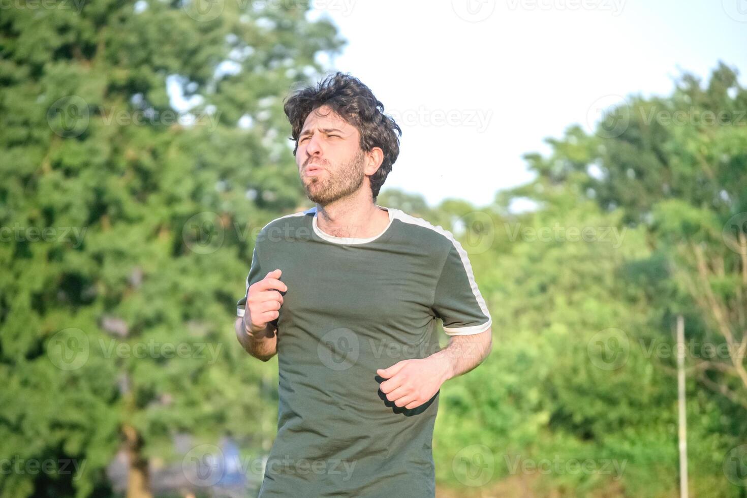Jeune homme avec vert T-shirt exercice et avec geste de Souffrance dans parc photo