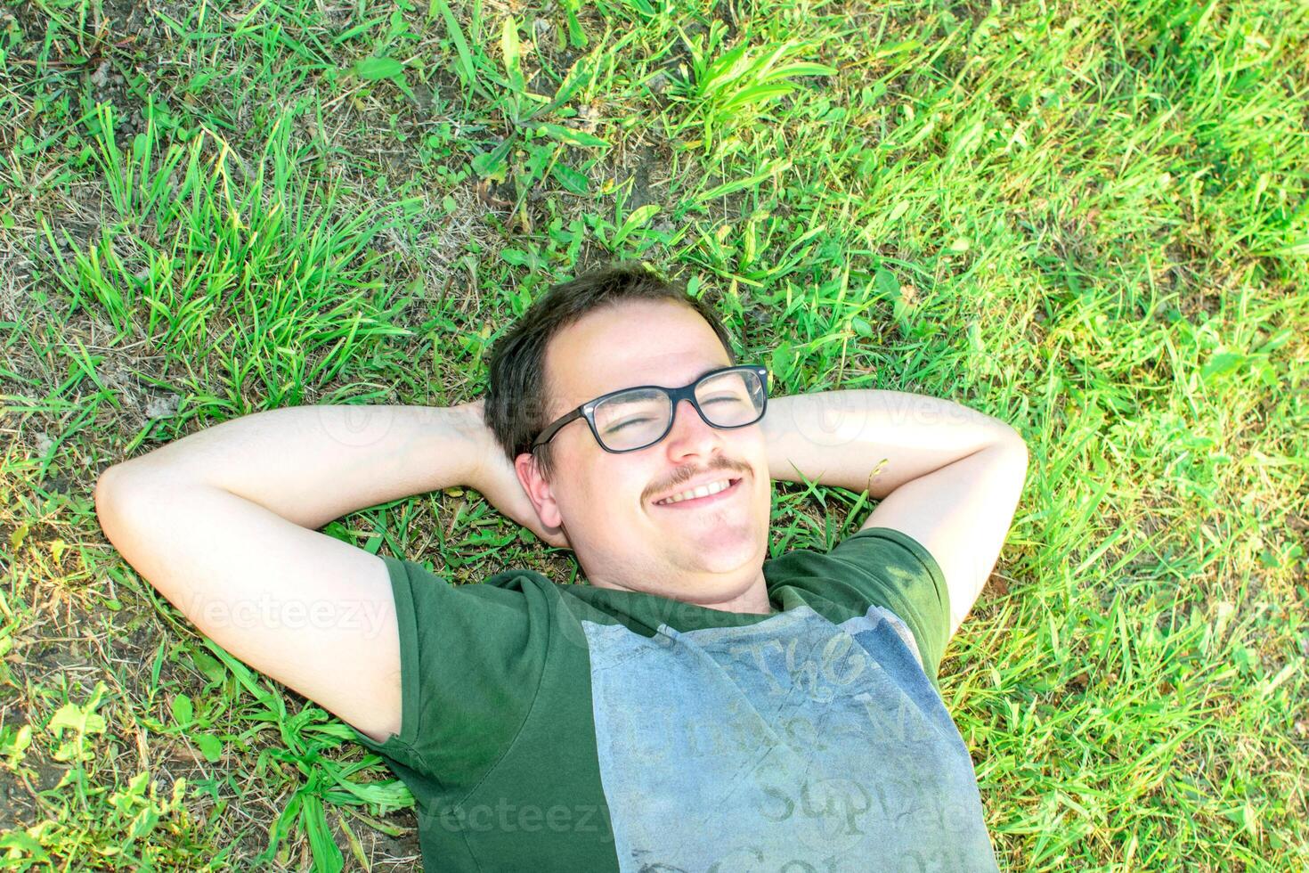 Jeune homme avec des lunettes menti sur herbe profiter vacances après en train d'étudier très content photo