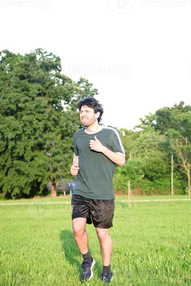 Jeune homme avec vert T-shirt exercice et avec geste de Souffrance dans parc photo