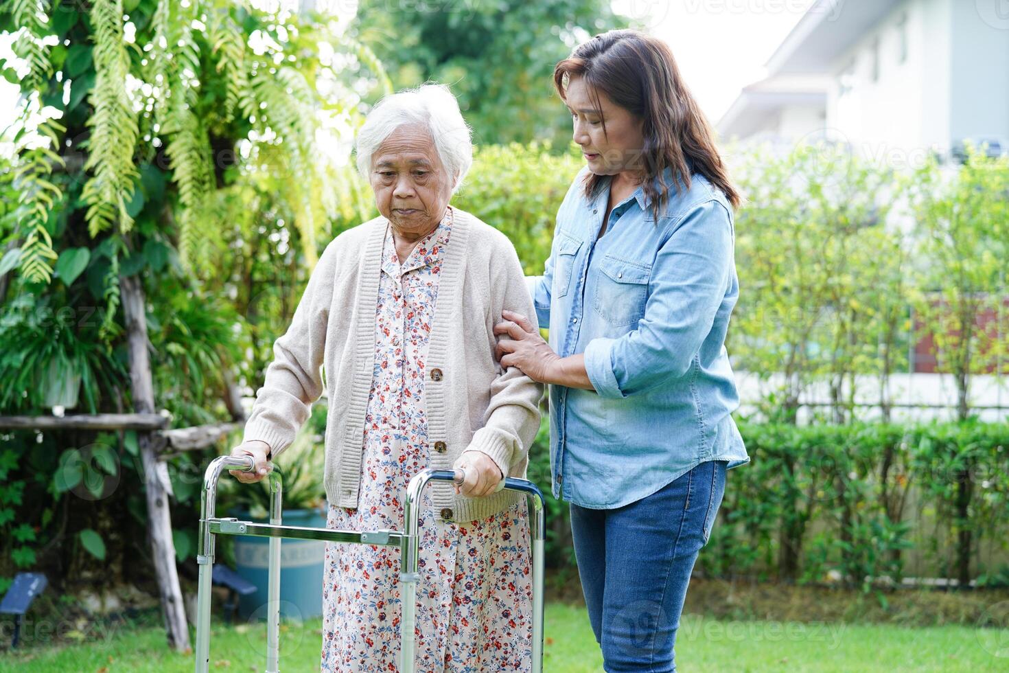 le soignant aide une femme âgée asiatique handicapée à marcher avec une marchette dans le parc, concept médical. photo