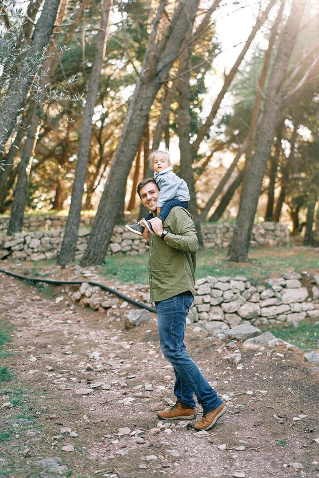 papa avec une peu fille sur le sien épaules des promenades à la recherche retour le long de le chemin dans le forêt photo