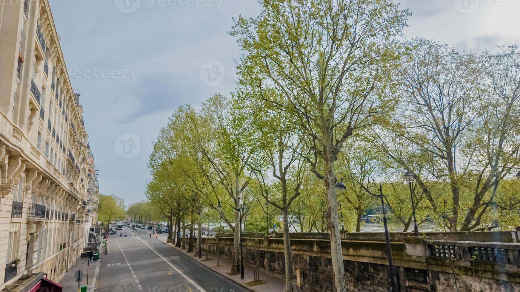 printemps vue de une serein Urbain rue doublé avec bourgeonnant des arbres, Parisien architecture, et une aperçu de une rivière, évoquant européen les vacances photo