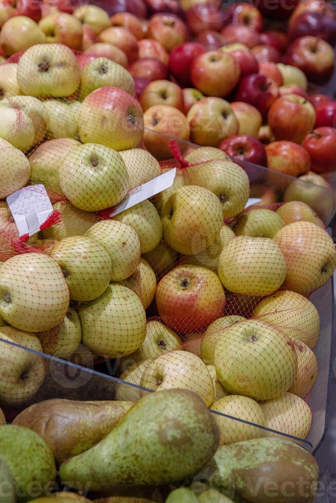 Frais poires et pommes dans rouge achats filet. des fruits arrangé dans le épicerie boutique sur le comptoir. vert des poires, pommes avec producteur Mots clés autocollants sur nourriture marché étagère. côté voir. sélectif se concentrer. photo