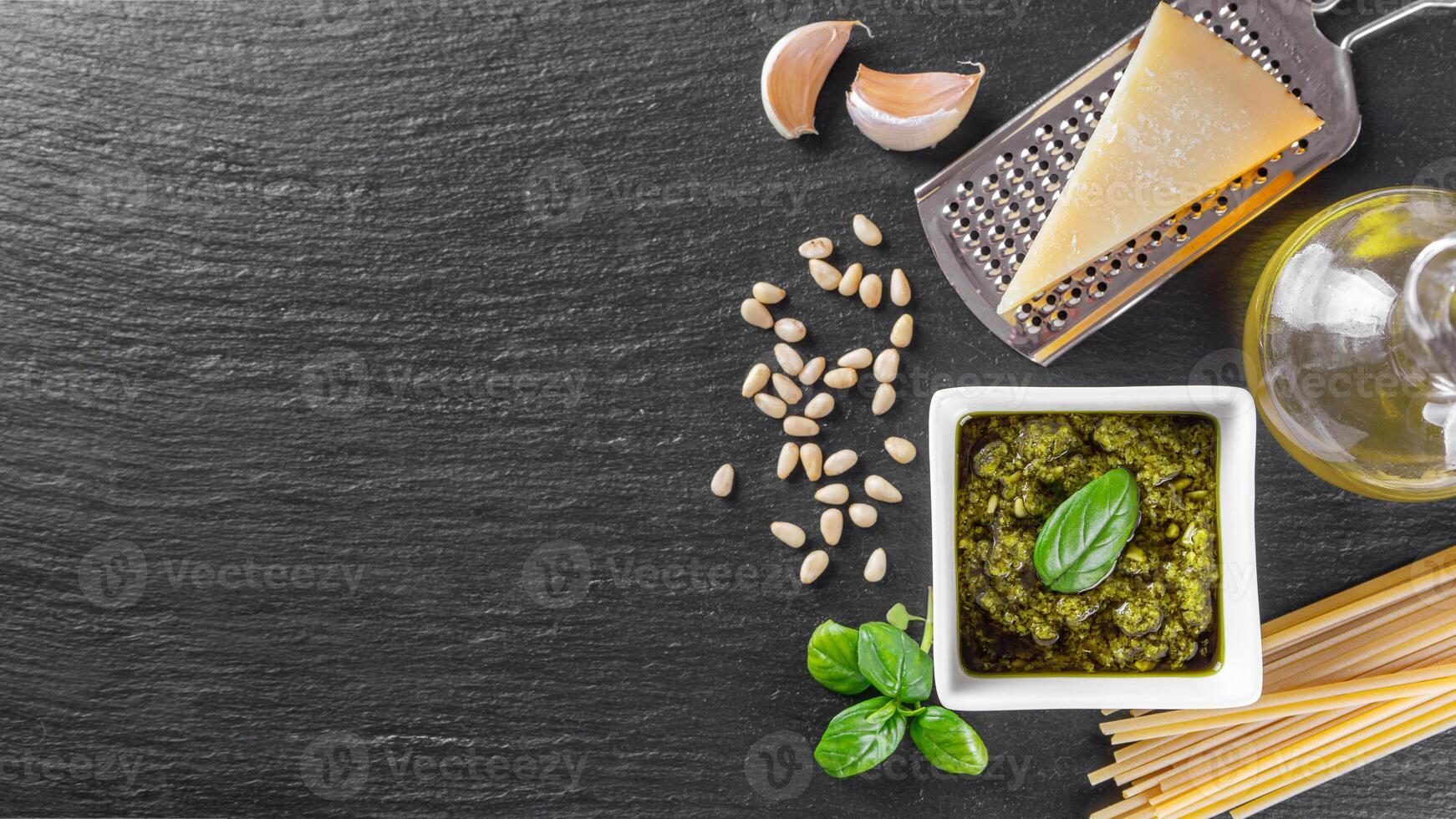 fait maison Pesto sauce dans petit blanc carré pot et Ingrédients pour Pâtes sur noir ardoise Contexte photo