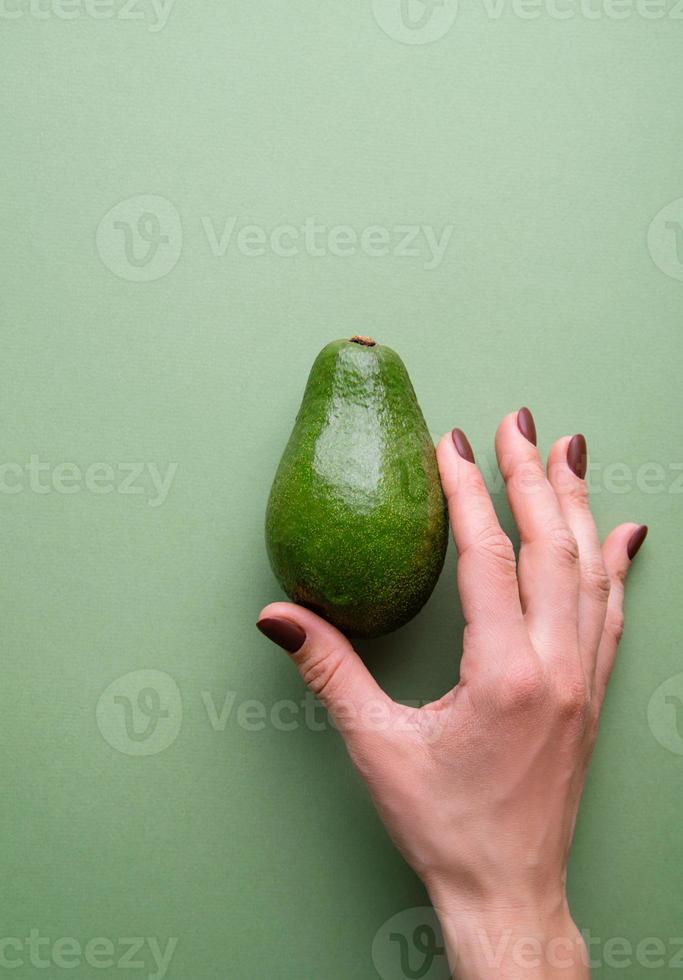 avocat entier dans une main sur la vue de dessus de fond vert photo