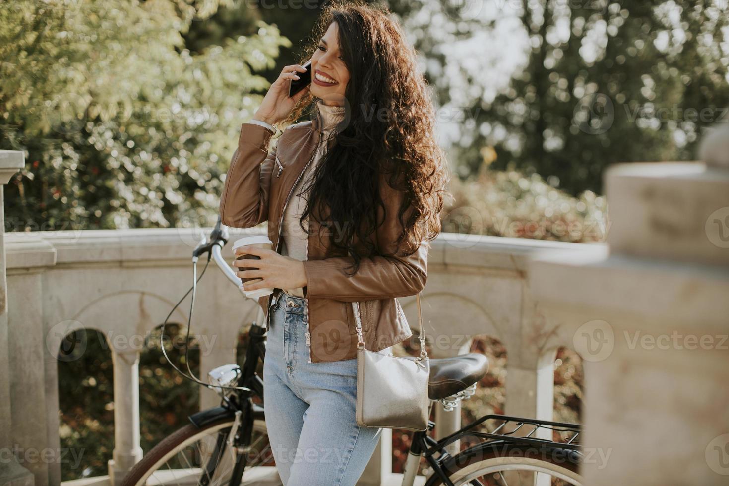 Jeune femme avec téléphone portable boire du café pour aller à vélo le jour de l'automne photo