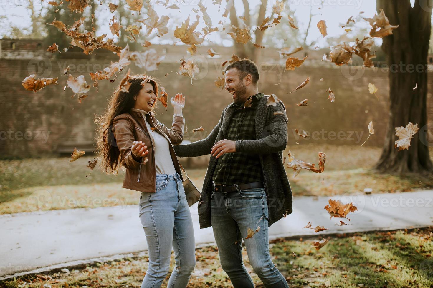 Jeune couple s'amusant avec des feuilles dans le parc d'automne photo