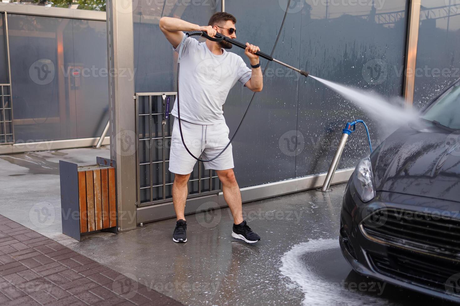 une homme lavages le de face de une voiture avec une l'eau canon. une voiture à une soi un service voiture laver. photo