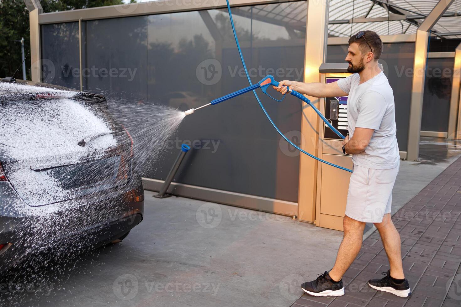 une homme détient une mousse pulvérisateur de lequel mousse mouches en dehors sur une auto. une voiture à une soi un service voiture laver. photo