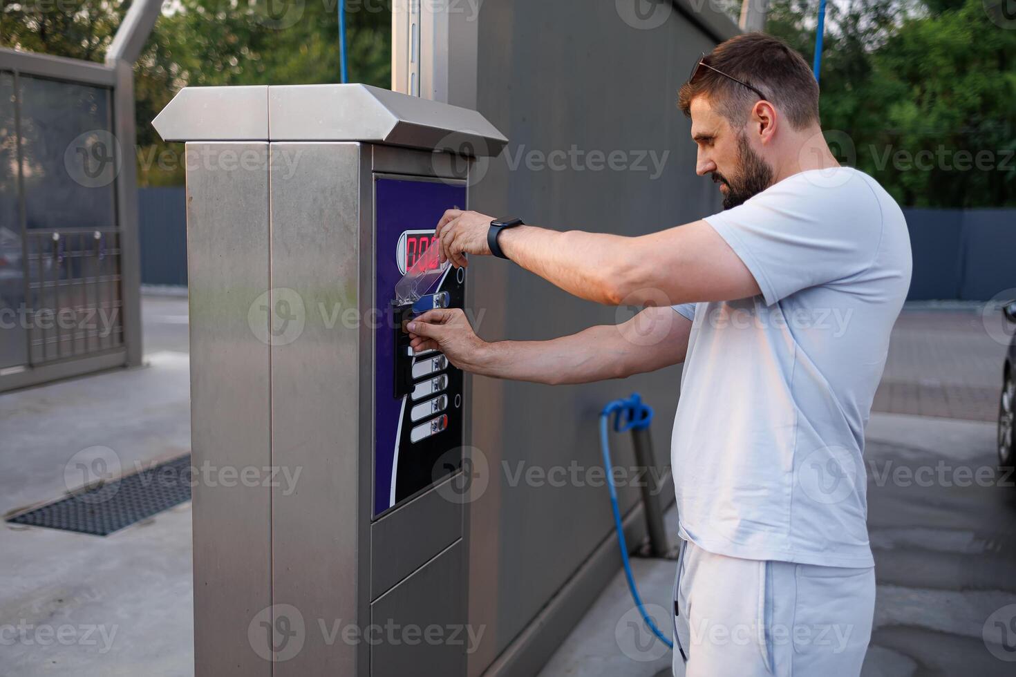 une homme jette une jeton dans une voiture laver machine. une voiture à une soi un service voiture laver. photo