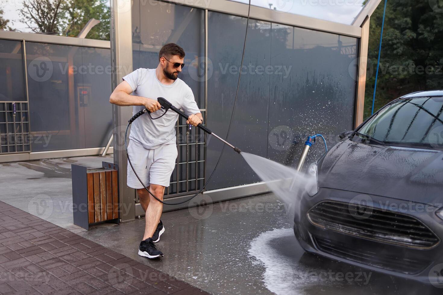 une homme lavages le de face gril de une voiture avec une l'eau canon. une voiture à une soi un service voiture laver. photo