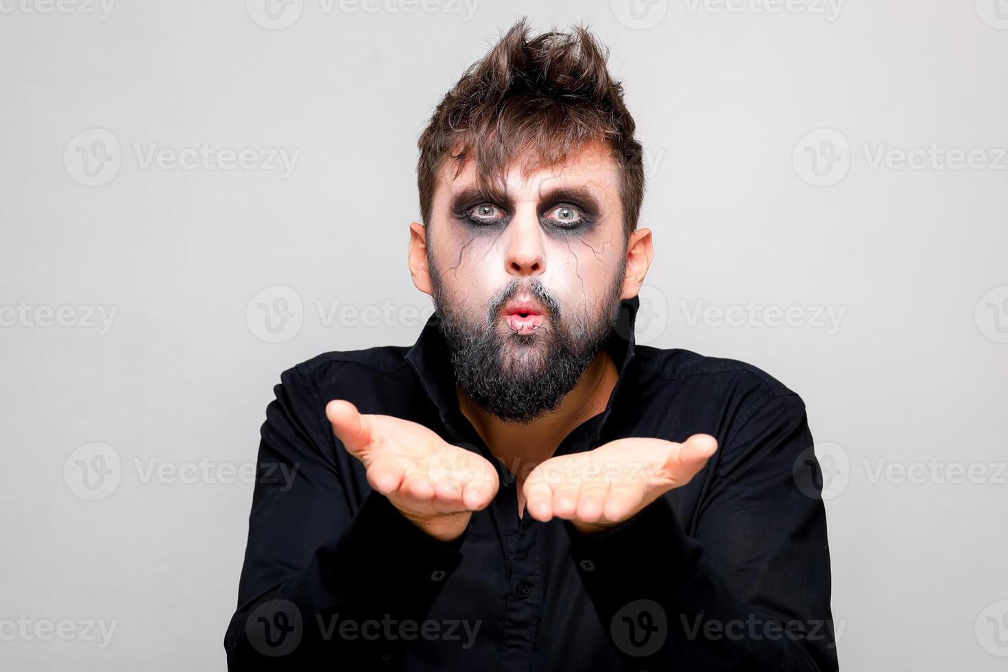 une homme avec une barbe et Mort-vivant maquillage sur Halloween détient le sien mains dans de face de lui photo