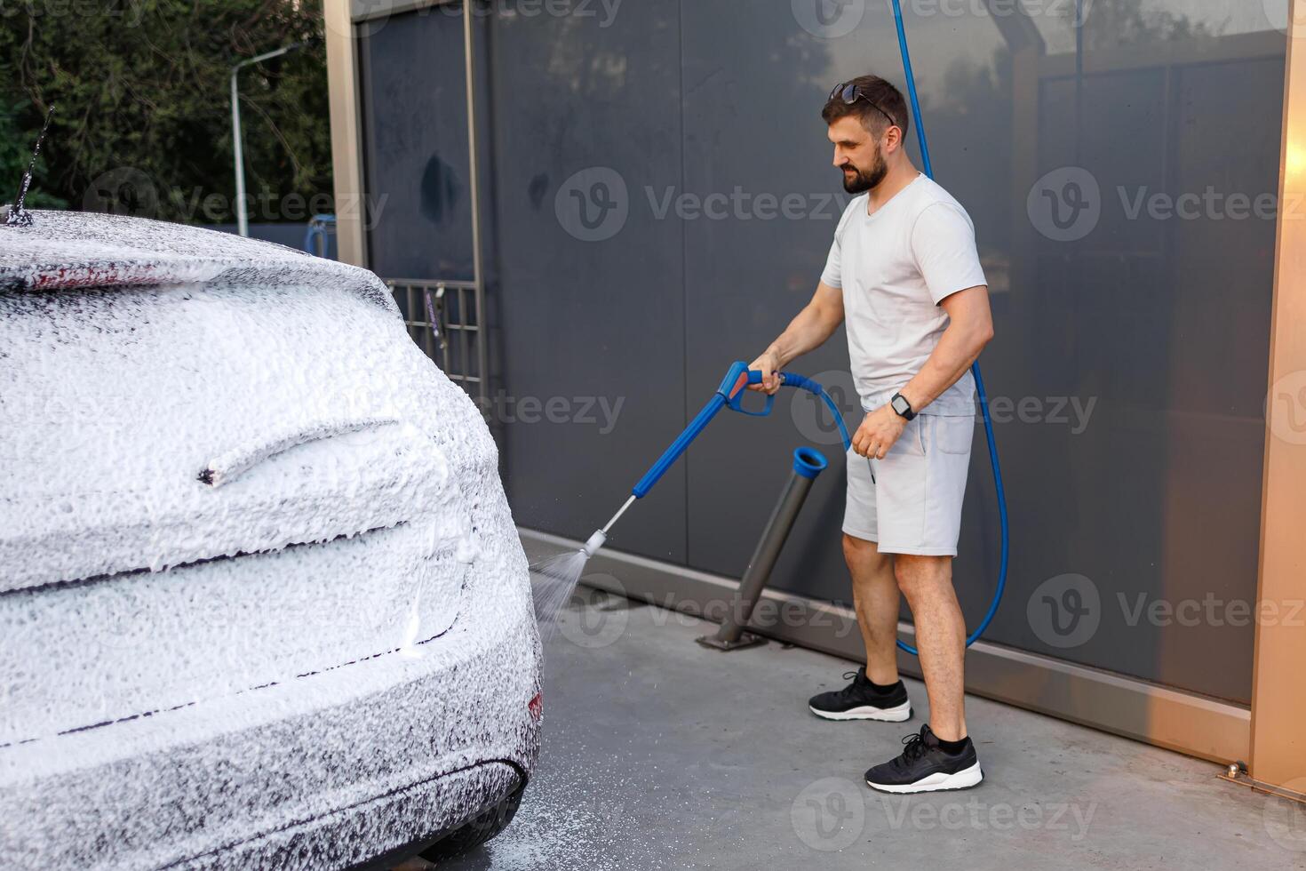 le arrière de le voiture est couvert avec mousse, le homme dans le Contexte est appliquant mousse à le auto. une voiture à une soi un service voiture laver. photo