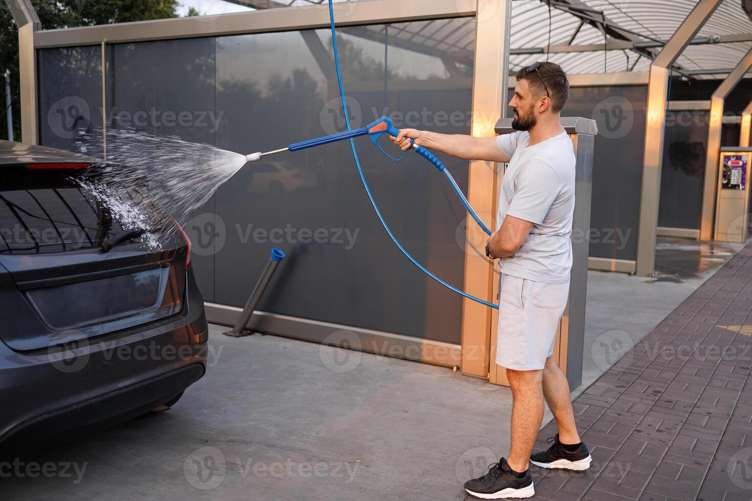 une homme points une mousse pulvérisateur à une auto. une voiture à une soi un service voiture laver. photo