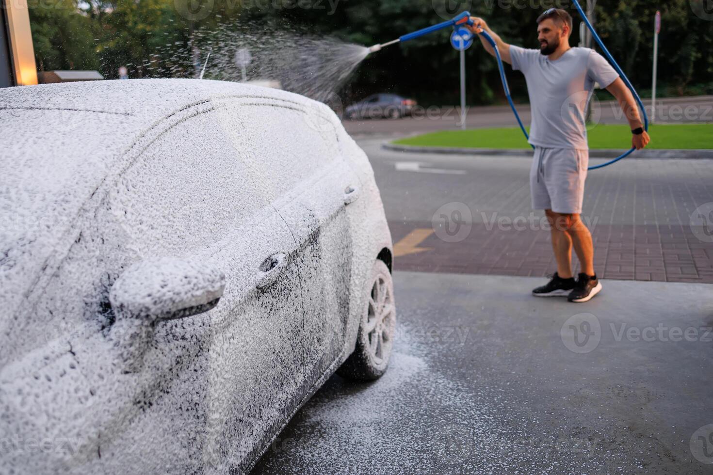 côté vue de une voiture couvert dans mousse, homme dans le Contexte appliquant mousse à le auto. une voiture à une soi un service voiture laver. photo