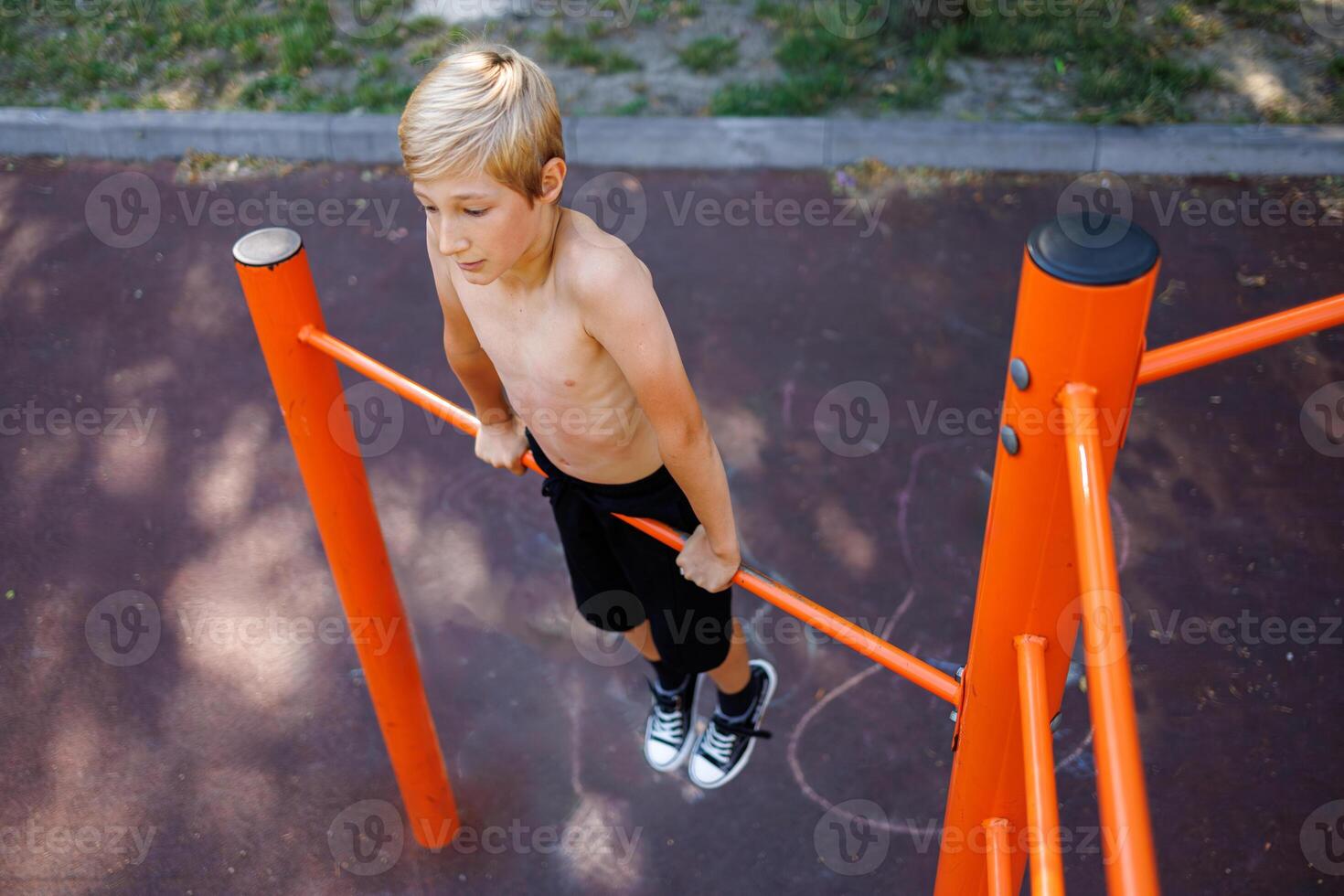 le adolescent étiré en dehors sur le sien mains et effectue acrobatique des exercices sur le horizontal bar. rue faire des exercices sur une horizontal bar dans le école parc. photo
