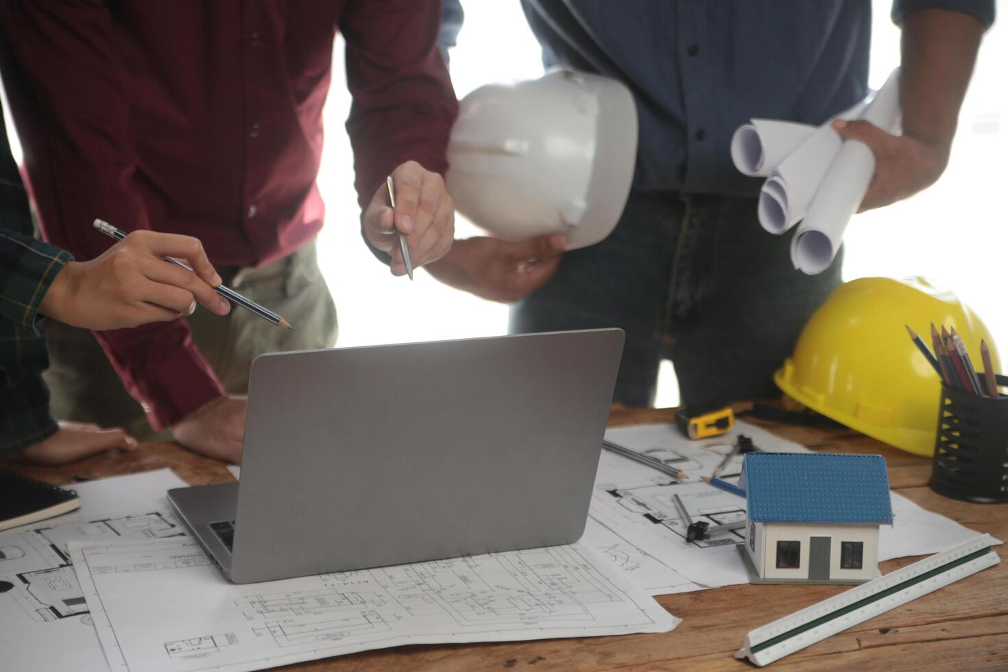 ingénieurs sont consultant le équipe à conception un architectural structure pour clients avec plans et bâtiment des modèles à travail à bureau. photo