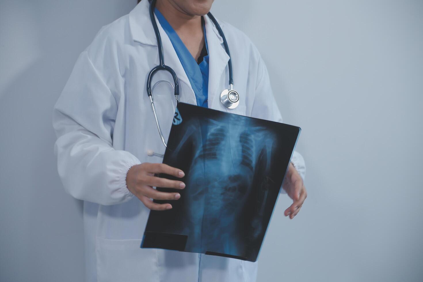 asiatique musulman médecin dans hijab et gommages écouteurs autour sa cou supporter en toute confiance dans le médical bureau, isolé sur blanc arrière-plan, en portant radiographie film. photo