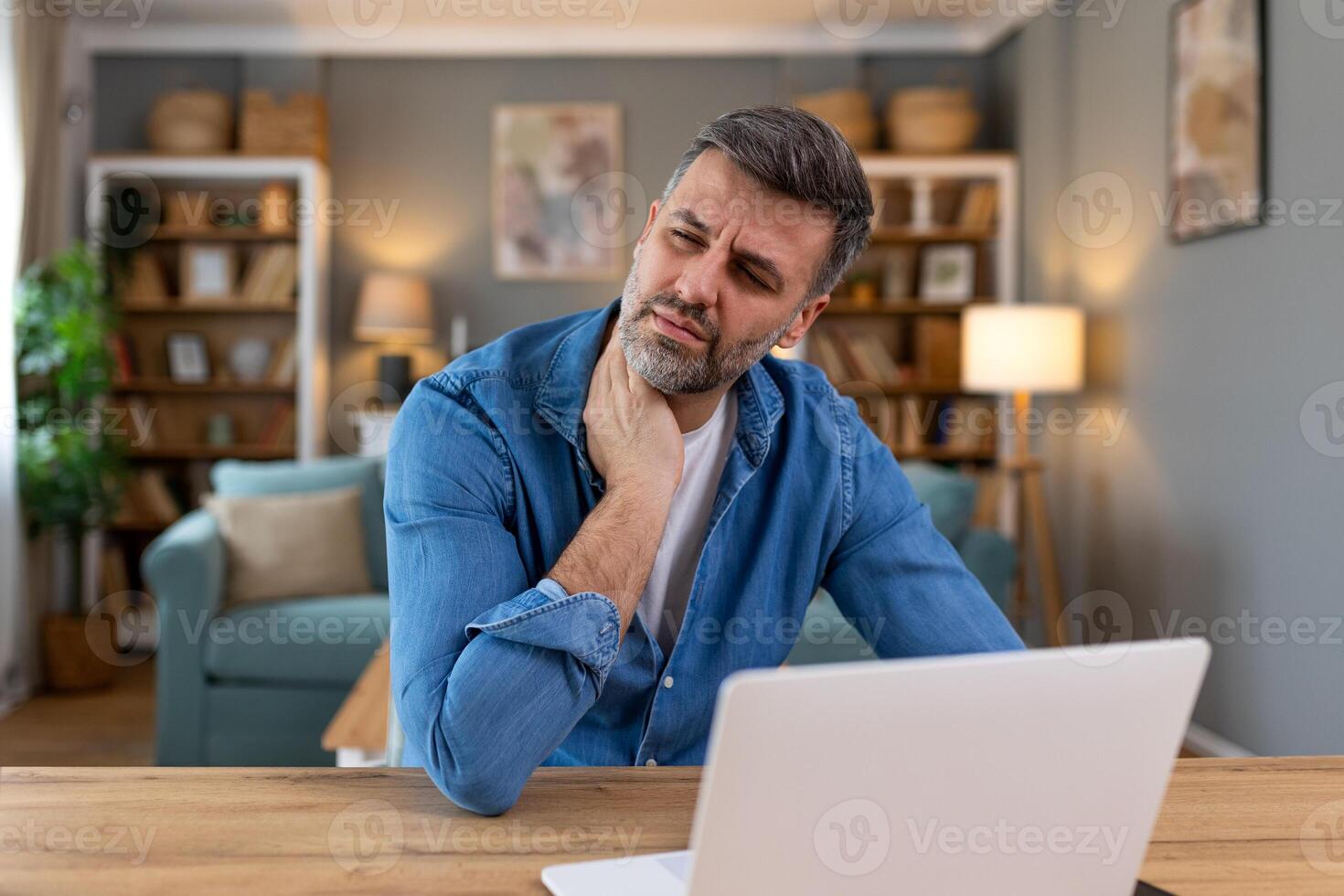 homme d'affaire sentiment douleur dans cou après séance à le table avec portable. fatigué homme Souffrance de Bureau syndrome car de longue heures ordinateur travail. il est masser le sien tendu cou muscles photo