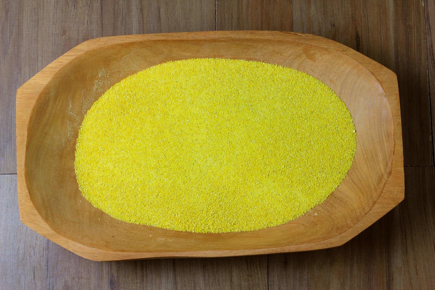 portion de farine de manioc crue jaune, bol en bois, vue de dessus de table en bois photo