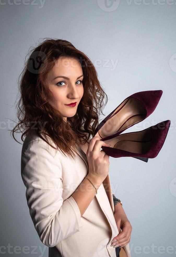 fille dans une veste beige et des chaussures dans ses mains, posant pour la caméra. photo